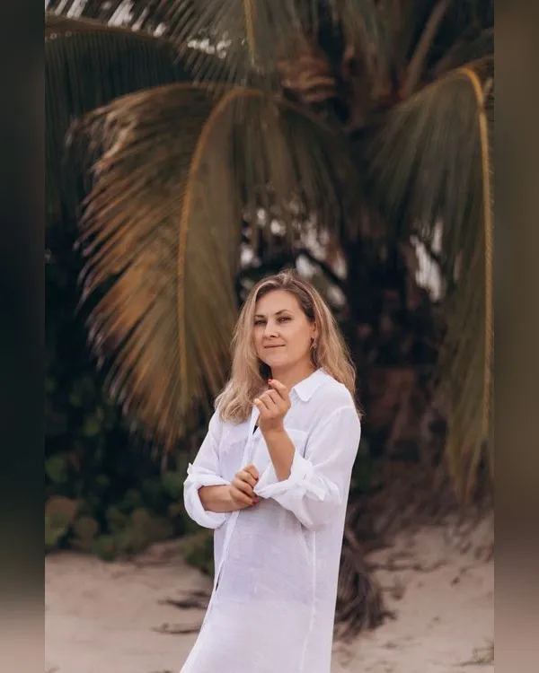 Olga, founder of Red Peony, wearing the white beach cover shirt by the palm trees